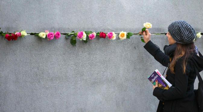Seorang wanita menempatkan kuntum mawar di dinding peringatan Tembok Berlin di sepanjang jalan Bernauer Strasse selama upacara menandai ulang tahun ke-26 runtuhnya Tembok Berlin, Jerman, Senin (9/11). (REUTERS/Hannibal Hanschke)