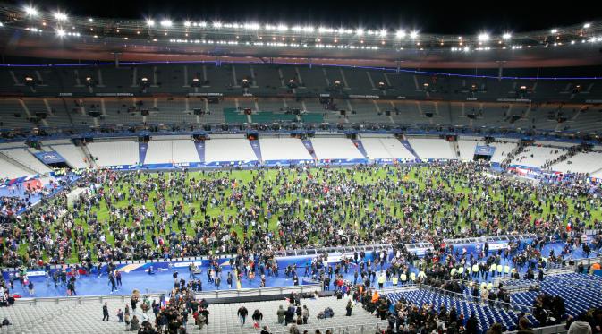 Ribuan Penonton berhamburan di lapangan stadion Stade de France saat menyaksikan pertandingan antara Prancis melawan Jerman di Saint-Denis, Paris, (13/11). Serangan bom terjadi di dekat stadion Stade de France Prancis. (AFP PHOTO/Matthieu ALEXANDRE).