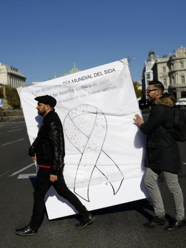 Dua laki-laki membawa gambar pita dengan tanda merah yang dibubuhkan warga, Madrid, Spanyol, Selasa (1/12)| via: Francisco Seco/AP Photo