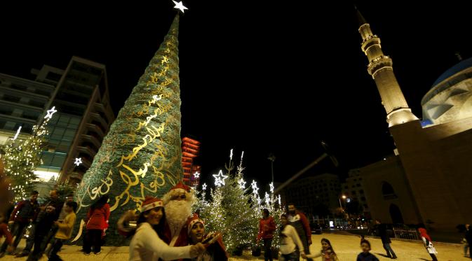 Seorang anak berselfie dengan pria berkostum Sinterklas dengan latar belakang pohon Natal yang dirancang oleh desainer Lebanon, Elie Saab di depan Masjid Al-Amin, di pusat kota Beirut, 12 Desember 2015. (REUTERS/Jamal Saidi)