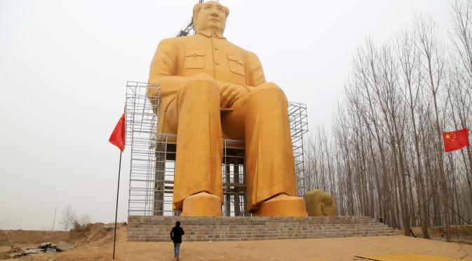 Seorang pria berada dibawah patung Presiden pertama Cina, Mao Zedong saat proses penyelesaian pembangunannya di ladang Desa Tongxu, Henan, Cina (4/1). Menurut warga, patung tersebut menghabiskan sekitar USD 460.000 atau Rp 6,4 miliar. (Reuters/Stringer)