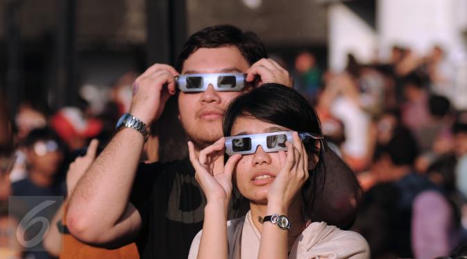 Sepasang muda mudi menggunakan kacamata khusus untuk melihat proses gerhana matahari di sekitar Taman Ismail Marzuki, Jakarta, Rabu (9/3/2016). Di Jakarta, fenomena gerhana matahari 90% bisa diamati selama 2,11 menit. (Liputan6.com/Helmi Fithriansyah)   