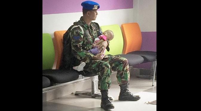 Sebuah foto diunggah di Instagram ini bikin banyak netizen baper. Terlihat seorang TNI menggendong dan menjaga anaknya. Duh, haru!