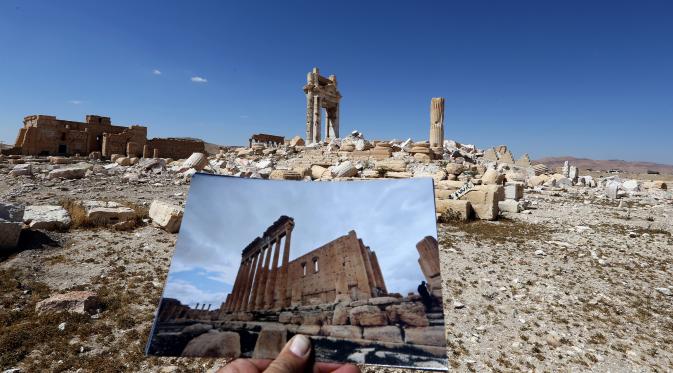 Fotografer bernama Joseph Eid memegang foto Temple of Bel yang diambil pada tanggal 14 Maret 2014 di depan sisa-sisa kuil bersejarah setelah dihancurkan oleh ISIS pada September 2015 di kota kuno Palmyra, Suriah, 31 Maret 2016. (Joseph EID/AFP)