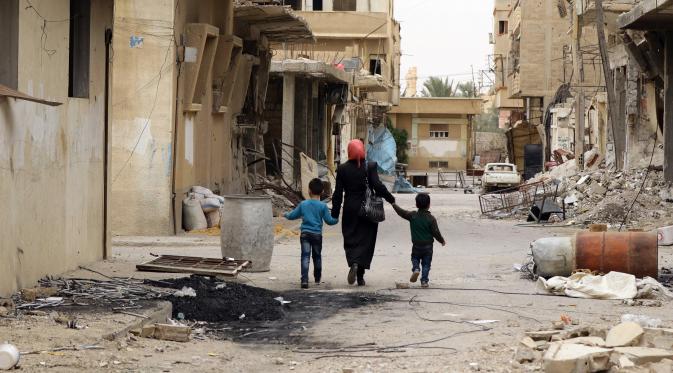 Seorang ibu bersama anaknya kembali ke rumah mereka di kota modern Palmyra, berdekatan dengan kota kuno Suriah, Sabtu (9/4). Kota itu berhasil direbut kembali oleh militer Suriah dari tangan kelompok ekstrimis ISIS beberapa waktu lalu. (Louai BESHARA/AFP)