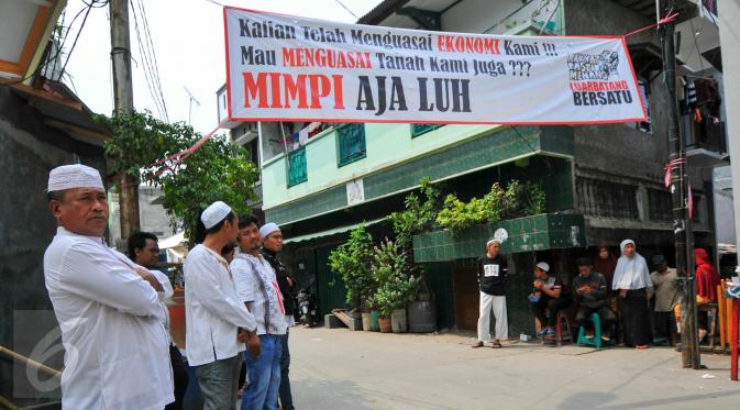 Sejumlah warga berdiri di bawah spanduk penolakan penggusuran Kampung Luar Batang, Penjaringan, Jakarta, Rabu (20/4). Mereka menolak pembongkaran tahap dua yang akan dilakukan Pemprov DKI pada Mei nanti. (Liputan6.com/Yoppy Renato)