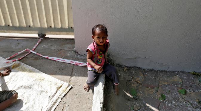 Shivani (15 bulan) duduk di tanah dengan kaki terikat pada batu di lokasi konstruksi di Ahmedabad, India, 20 April 2016. Ibunya, Sarta Kalara mengaku tak memiliki cara lain kecuali mengikatkan buah hatinya ke batu meskipun dia menangis (REUTERS/Amit Dave)