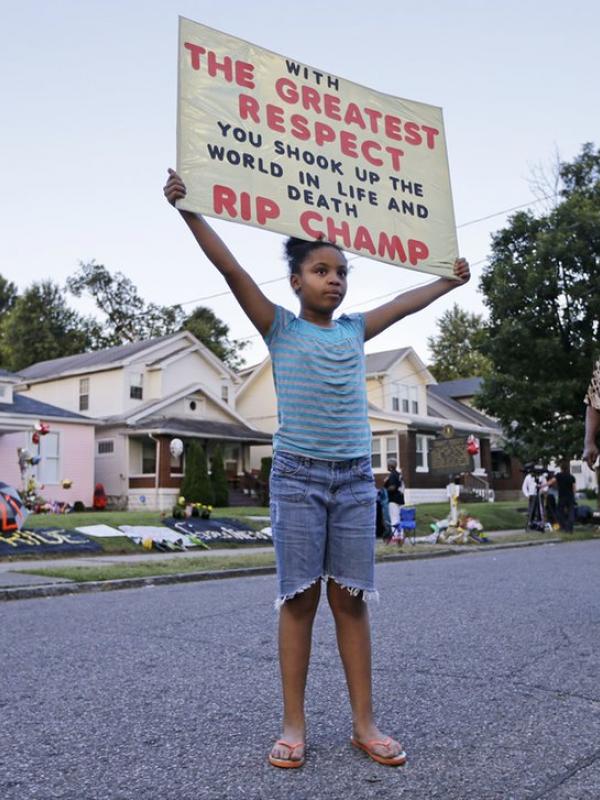 Anak berusia 9 tahun membawa banner di depan rumah kecil Muhammad Ali. (Mark Humphrey/AP)