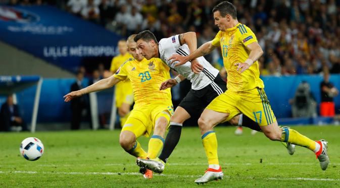 Gelandang Jerman, Mesut Ozil (tengah) berusaha melewati dua pemain Ukraina di kualifkasi grup C Piala Eropa 2016 di Stadion Stade Pierre-Mauroy, Perancis, (12/6). Jerman menang atas Ukraina dengan skor 2-0. (REUTERS/Gonzalo Fuentes)