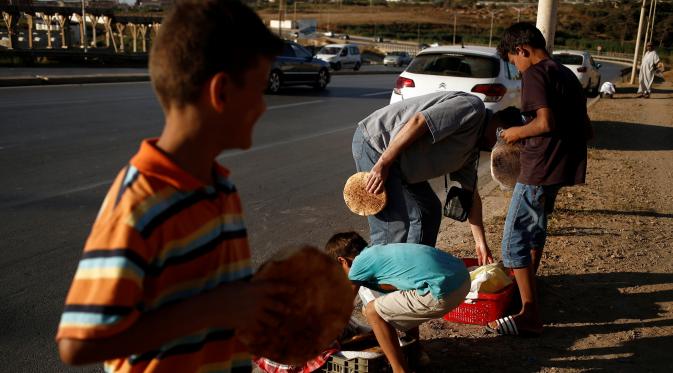 Seorang pembeli membeli roti tradisional yang dijajakan salah satu bocah di tepi jalan raya di pinggiran Algiers, Aljazair, 13 Juni 2016. Selama bulan Ramadan, sejumlah anak membantu orangtuanya menjajakan roti di kawasan ini. (REUTERS/Zohra Bensemra)