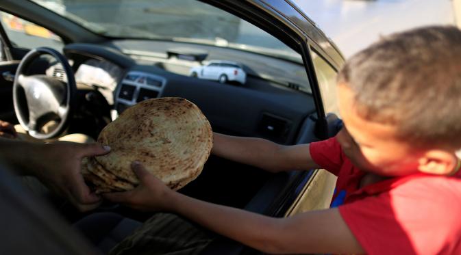 Issaac (8), menjual roti tradisional dagangannya kepada seorang pembeli di pinggiran Algiers, Aljazair, 13 Juni 2016. Selama bulan Ramadan, sejumlah anak membantu orangtuanya menjajakan roti di kawasan ini. (REUTERS/Zohra Bensemra)