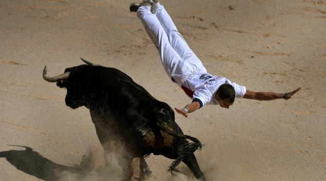 Seorang recortador melompati serudukan banteng selama Festival San Fermin di Pamplona, Spanyol, Sabtu (9/7). Aksi akrobatik melompati serangan banteng ini dinamakan recortadores. (REUTERS / Vincent West)