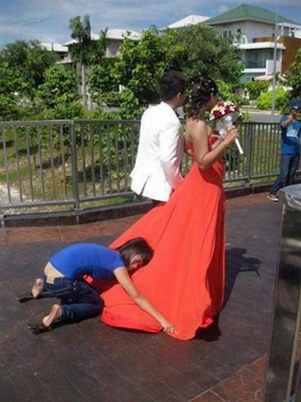 Seorang asisten fotografer yang rela berjongkok di belakang pengantin wanita demi membuat gaun pengantin yang dipakai terlihat indah di foto. Sumber : mymodernmet.com
