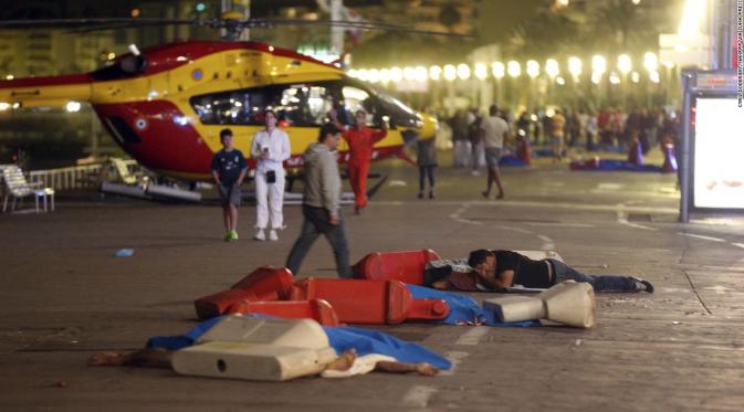 Seorang lelaki terlihat berbaring di samping tubuh yang sudah ditutupi di Nice, Perancis, saat perayaan Bastille Day. (CNN)