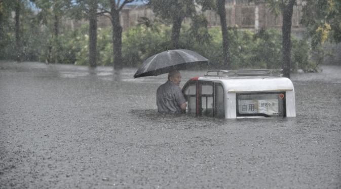 Pria terjebak di samping kendaraannya yang terjebak banjir di Beijing (Reutes)