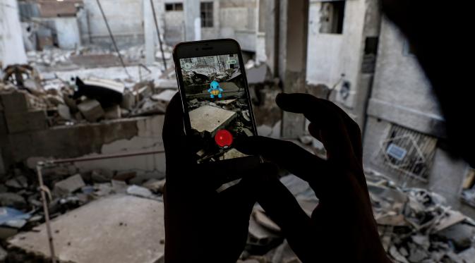 Seorang gamer Suriah menggunakan aplikasi Pokemon Go di ponselnya untuk mencari Pokemons di antara puing-puing di kota Douma, Damaskus (23/7). (AFP PHOTO / Sameer Al-Doumy)