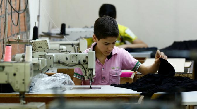 Bocah pengungsi Suriah bernama Muhamed saat menjahit kain di sebuah pabrik tekstil, Istanbul, Turki, (24/6). Meski seumurannya masih menikmati bangku sekolah, mereka menikmati pekerjaan mereka. (REUTERS/Murad Sezer)