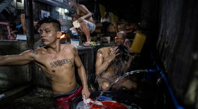 Narapidana memasak makan malam sementara kawannya mandi di dalam penjara Quezon City di Manila, Filipina, 21 Juli 2016. Kondisi sanitasi penjara Quenzon City sangat buruk, hanya terdapat satu toilet yang digunakan hingga 130 narapidana. (Noel Celis/AFP)