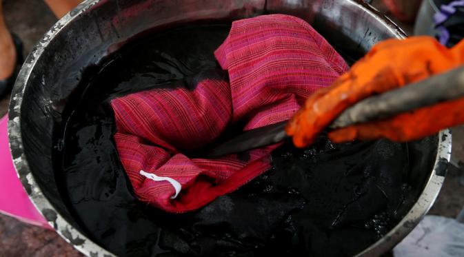 Pakaian dimasukan kedalam wadah untuk di warnai agar menjadi hitam, Bangkok, Thailand (17/10). Karena banyaknya kebutuhan warga untuk mengenakan pakaian hitam, relawan di Bangkok melayani pewarnaan pakaian secara gratis.(Reuters/Edgar Su)