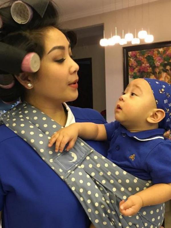 Nagita Slavina memakai rol rambut saat menggendong Rafathar. Foto tersebut diunggah ibunya, Rieta Amilia, pada 14 April 2016 (Instagram/@rieta_amilia)