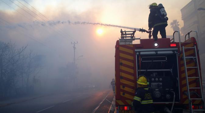 Petugas pemadam kebakaran menyemprotkan air ke arah hutan yang terbakar di kawasan Haifa, Israel, Kamis (24/11). Sekitar 50 persen dari kebakaran itu diduga disebabkan oleh aksi pembakaran yang disengaja. (REUTERS / Baz Ratner)