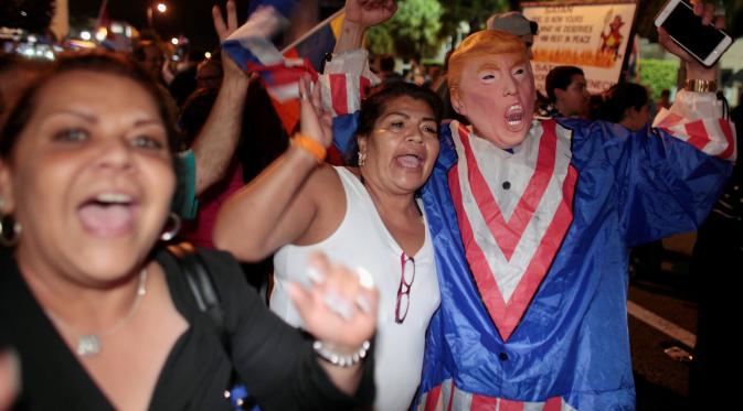 Warga kuba mengenakan kostum berwajah Donald trum saat turun ke jalan merayakan wafatnya Fidel Castro di Miami, AS (26/11). (REUTERS/Javier Galeano)