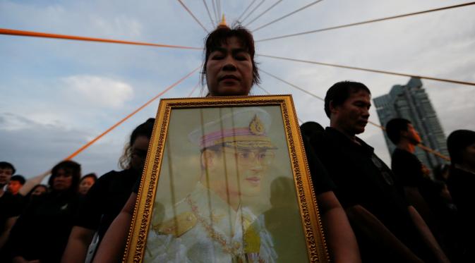 Warga membawa foto Raja Thailand, Bhumibol Adulyadej saat merayakan HUT terakhir almarhum di atas Jembatan Bhumibol, Bangkok, Thailand, Senin (5/12). Raja Bhumibol meninggal di usia 88 tahun. (REUTERS/Jorge Silva)