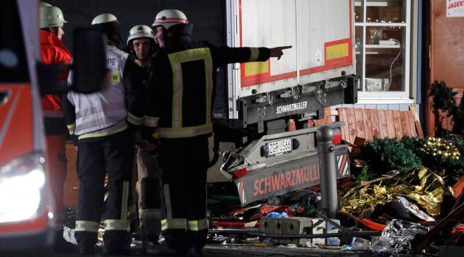 Petugas pemadam berdiri di dekat truk yang menabrak kerumunan orang di sebuah pasar Natal di pusat Kota Berlin, Jerman, Senin (19/12). Laporan-laporan menyebutkan supir truk sudah ditangkap sementara seorang penumpang tewas. (REUTERS/Pawel Kopczynski)