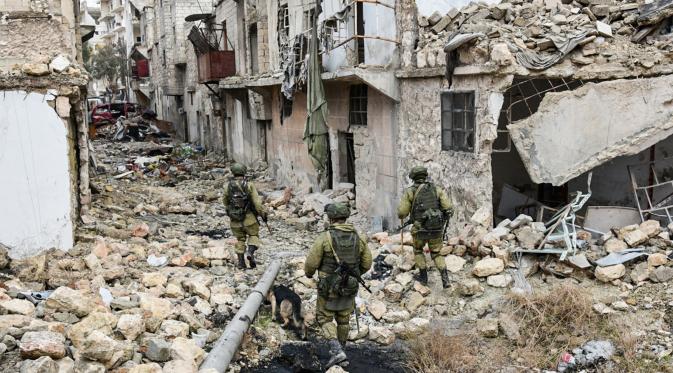 Para tentara Rusia berjalan di tengah bangunan yang rusak saat melakukan patroli dalam operasi APCs di Aleppo, Suriah. (Russian Defense Ministry Press Service photo via AP)