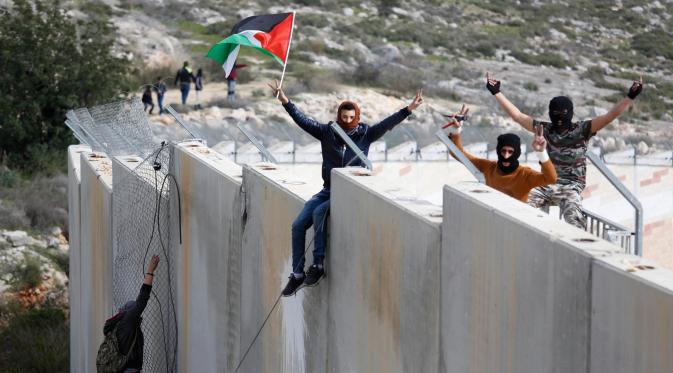 Pengunjuk rasa Palestina memanjat tembok pemisah dengan Israel saat aksi di desa Tepi Barat Bilin dekat Ramallah, Jumat (17/2). Aksi tersebut untuk memperingati 12 tahun protes mereka atas tembok pemisah tersebut. (AP Photo / Majdi Mohammed)