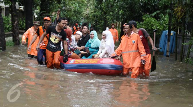 Keluarga pengantin Maya di evakuasi pasukan orange usai melakukan akad nikah di KUA Mampang Prapatan, Jakarta, Selasa (21/2). Walaupun banjir sepasang pengantin ini tetap melakukan akad nikah. (Liputan6.com/Herman Zakharia)