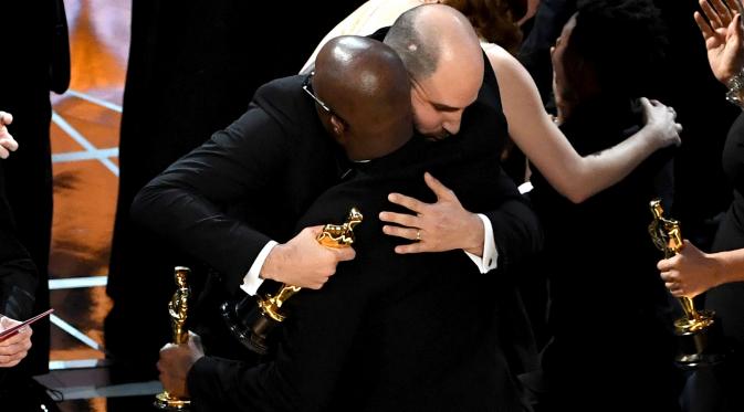 Produser La La Land, Jordan Horowitz (kiri) berpelukan dengan sutradara Moonlight, Barry Jenkins usai kesalahan pembacaan pemenang film terbaik di ajang Oscar 2017 di Hollywood, California, AS (26/2). (AFP/Getty Images/Kevin Winter)