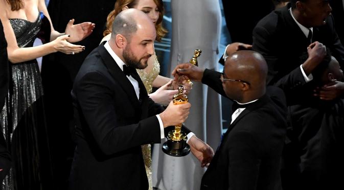 Produser La La Land, Jordan Horowitz (kiri) menyerahkan piala Oscar kepada sutradara Moonlight, Barry Jenkins usai kesalahan pembacaan pemenang film terbaik di ajang Oscar 2017 di Hollywood, California, AS (26/2). (AFP/ Getty Images/Kevin Winter)