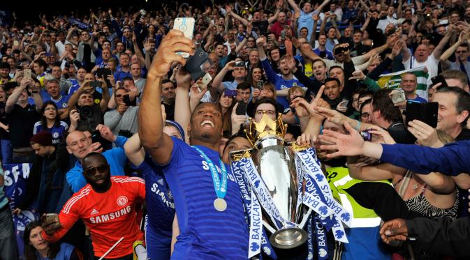 Penyerang Chelsea, Didier Drogba terlihat berselfie dengan pendukung Chelsea saat perayaan gelar juara Premier League 2014-15 di Stamford Bridge, Minggu (24/5/2015). Ini merupakan trofi pertama Thibaut Courtois di Premier League. (Reuters/Adam Holt )