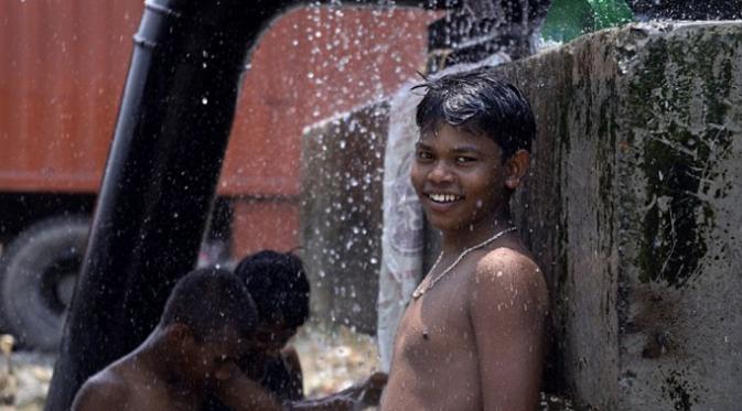 Seseorang bocah lelaki tersenyum di sebelah temannya yang sedang mandi di bawah percikan air (Via: dailymail.co.uk)