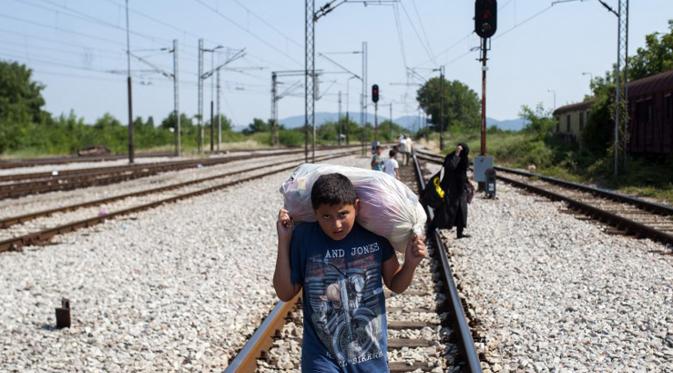 Seorang anak berjalan dengan membawa barang menyusuri rel kereta api saat perjalanan menuju Gevgelija, wilayah perbatasan Macedonia-Yunani, Kamis (9/7/2015). Mereka mencari perlindungan dengan menempuh ribuan kilometer. (AFP PHOTO/Robert ATANASOVSKI)