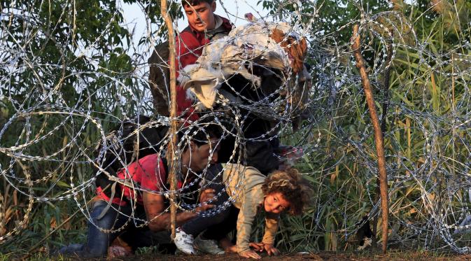 Seorang anak dibantu imigran Suriah berusaha melewati pagar berduri di wilayah Hungaria dekat perbatasan Serbia, wilayah Roszke, Kamis (27/8/2015). Hungaria berencana memperketat perbatasan bagian selatannya dari para pengungsi. (REUTERS/Bernadett Szabo)