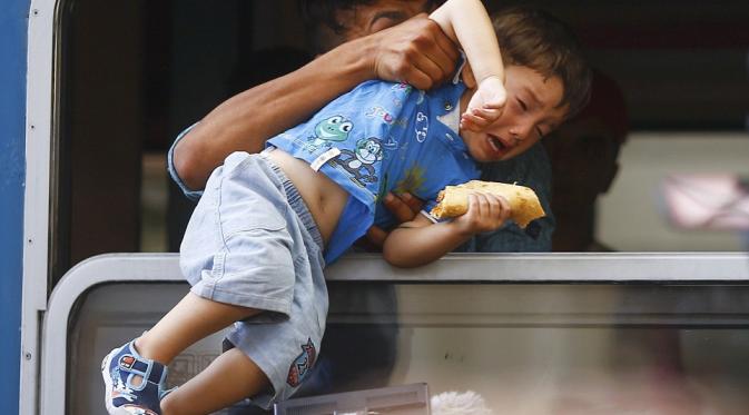 Seorang anak menangis saat dipaksa masuk ke jendela kereta. Berjam-jam mereka menunggu kapan kereta berangkat. Tapi Hungaria bersikukuh tidak akan mengirim mereka lagi untuk lebih jauh ke Eropa (Reuters)