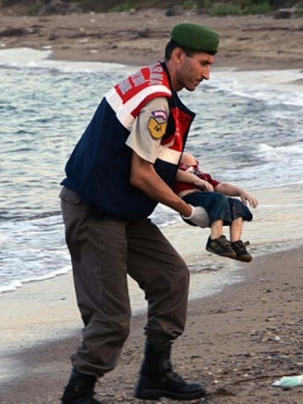 Petugas mengankat jenazah Aylan Kurdi. | via: theguardian.com
