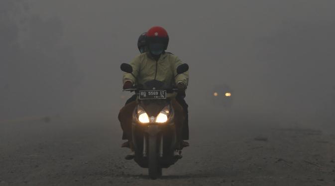 Pengendara motor menerobos jalan berkabut asap di jalan dekat pelabuhan Tanjung Siapi Api, Palembang, Sabtu (19/9/2015). Kabut asap akibat kebakaran hutan ini sangat membahayakan kesehatan dan keselamatan. (Reuters/Beawiharta)