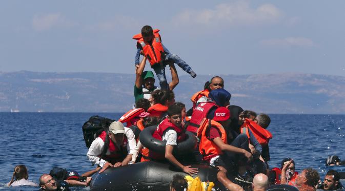 Seorang pengungsi mengangkat anaknya saat perahu mereka kempes di Pulau Lesbos, Yunani (13/9/2015). Menurut Organisasi Internasional untuk Migrasi (IMO) diperkirakan 309.000 orang telah tiba melalui laut di Yunani (REUTERS / Alkis Konstantinidis)